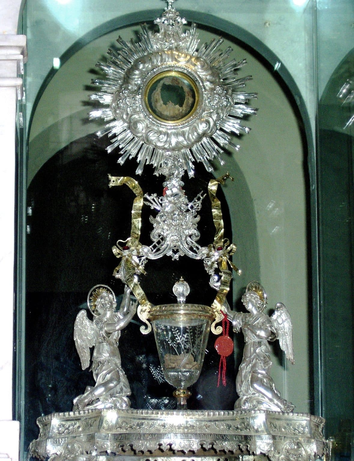 An ornate silver monstrance containing the Flesh of the Eucharistic Miracle of Lanciano, displayed behind glass.