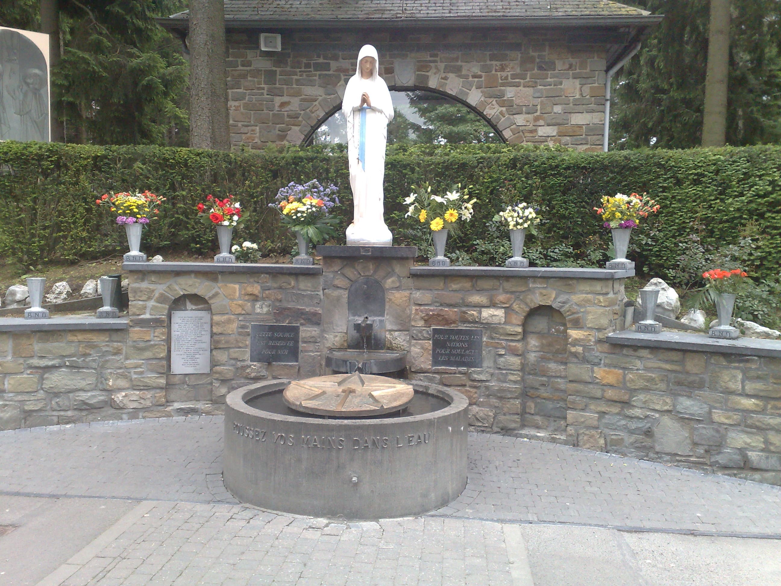 The stone statue of Mary, Virgin of the Poor, above the small spring at the Banneux sanctuary, Belgium — focal point of the 1933 apparitions.