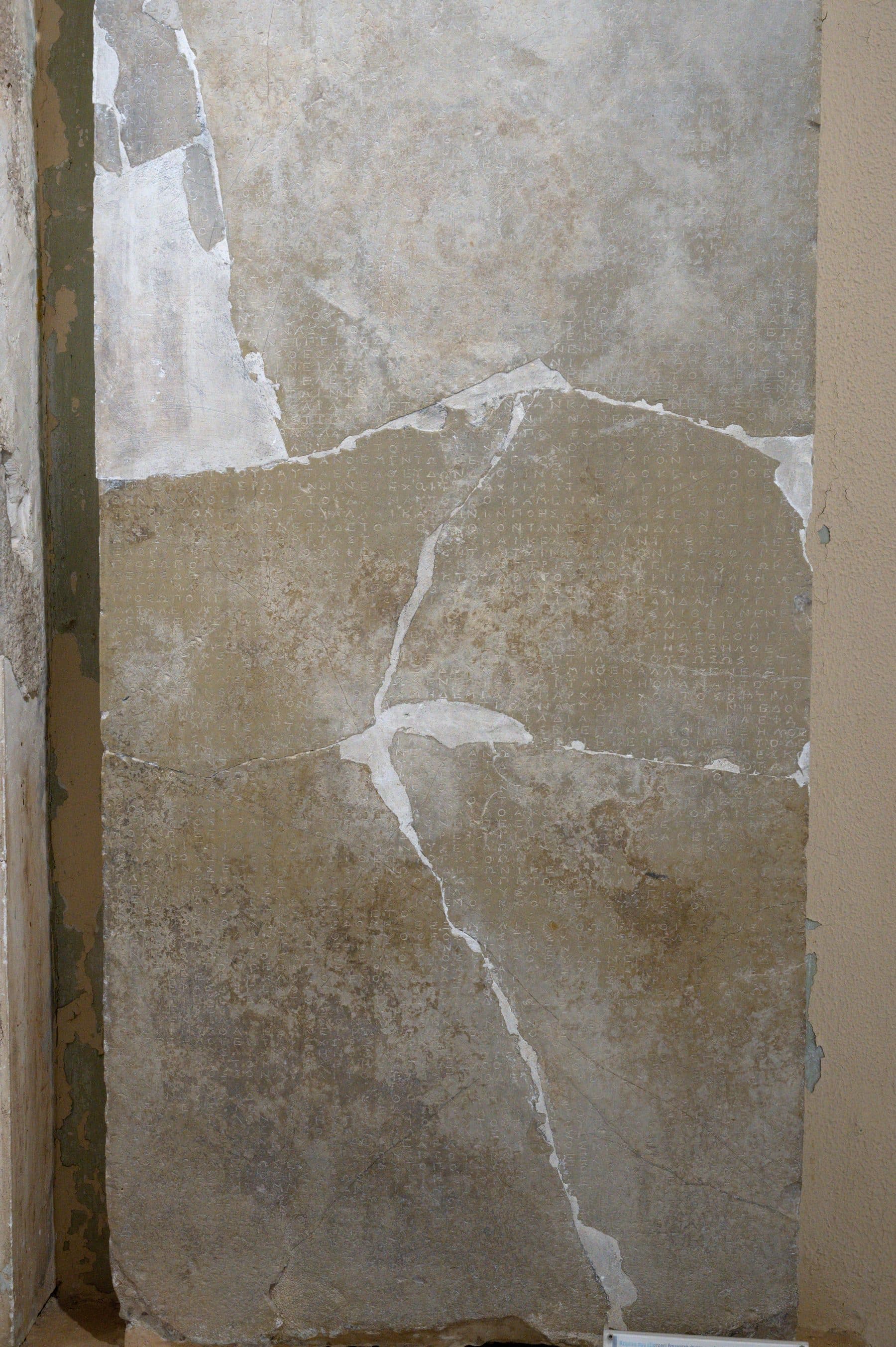 A weathered ancient Greek marble stele densely carved with inscription recording the miraculous cures of Asclepius, in the Archaeological Museum of Epidaurus.
