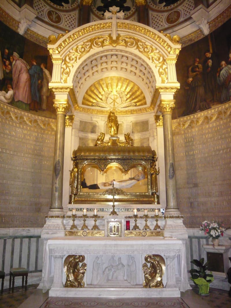 The body of St John Vianney in priestly vestments lying within a gilded glass reliquary châsse above the high altar in the Basilica of Ars, France.