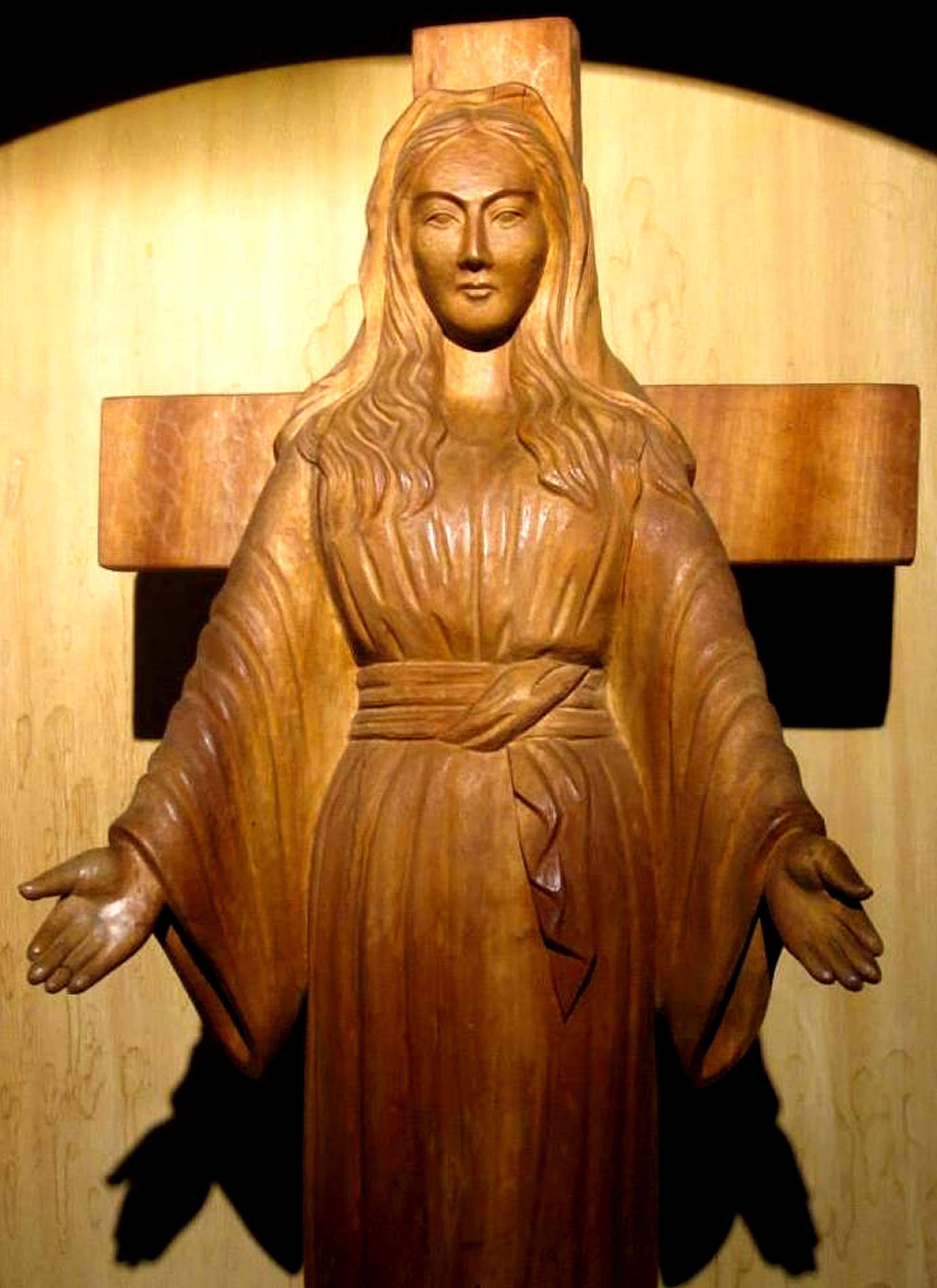 The carved light-wood statue of Our Lady of Akita with open hands, standing before a wooden cross at the convent in Akita, Japan.