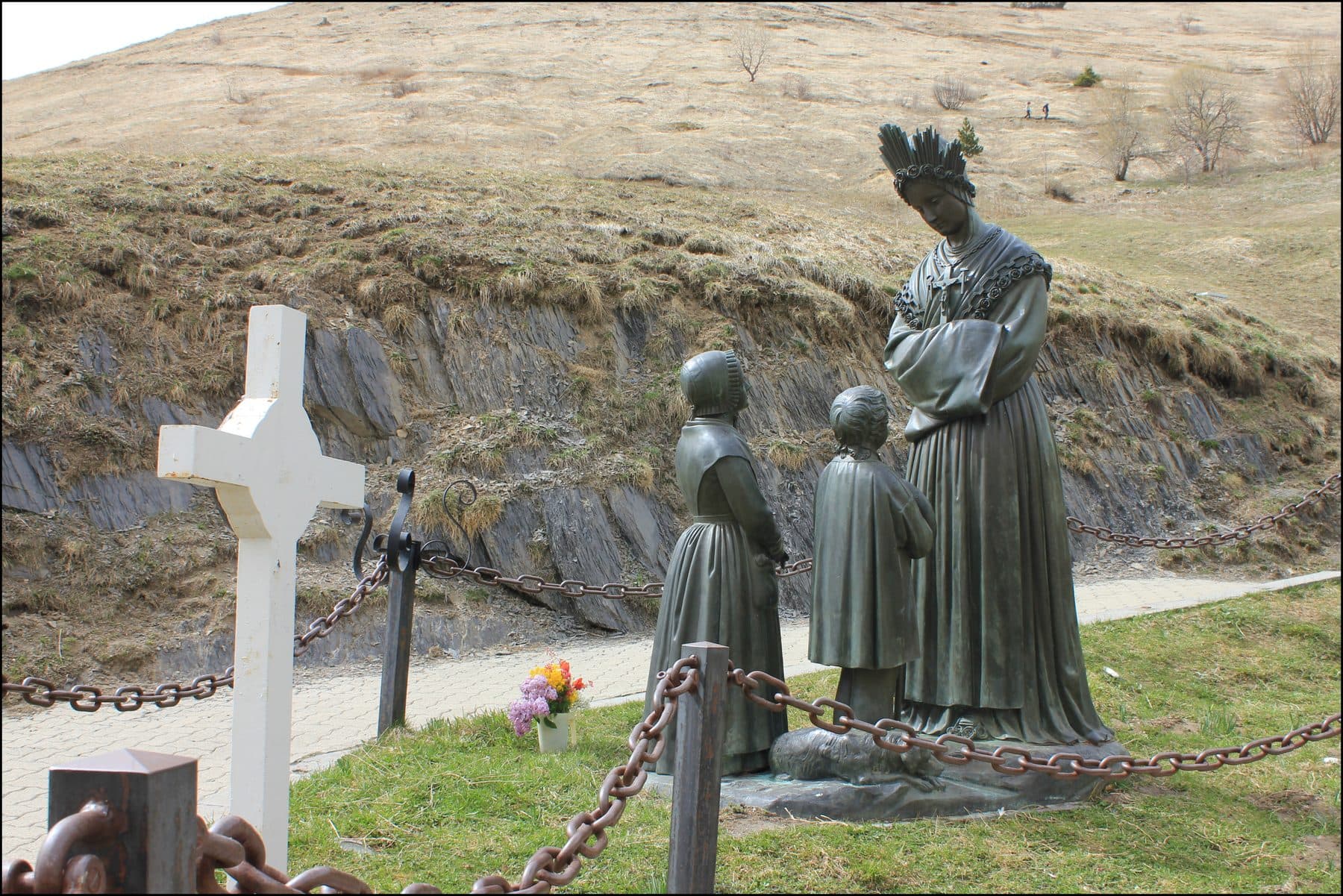 The bronze statue group at the La Salette apparition site in the French Alps: the weeping Virgin Mary addressing the two shepherd children, with a white cross alongside.