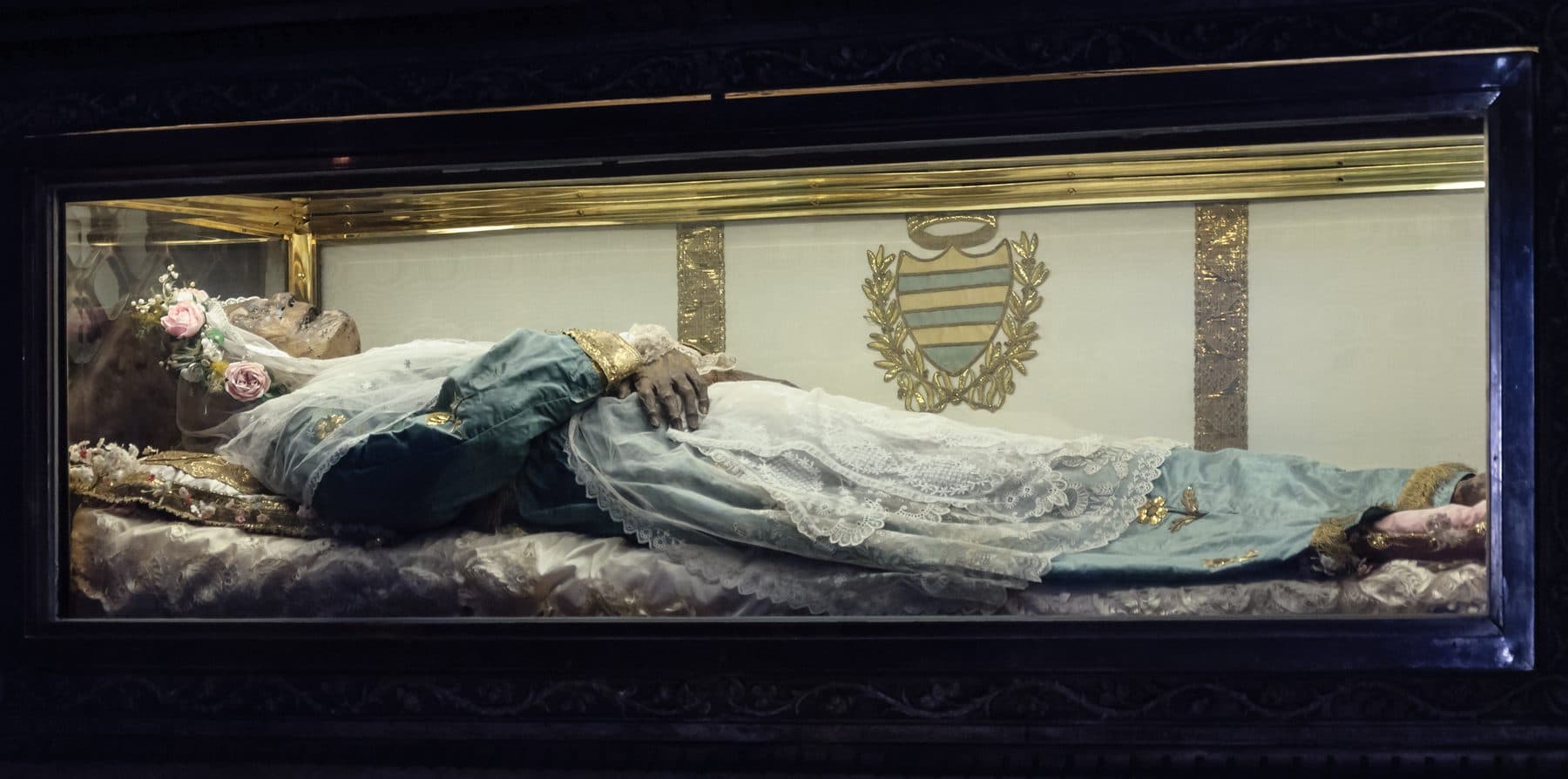 The naturally-mummified body of St Zita, robed with face and hands visible, in a gilded glass-fronted reliquary in the Basilica of San Frediano, Lucca.